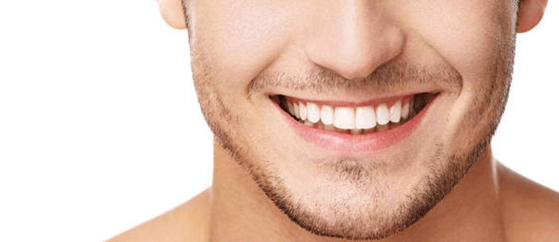 Close-up of the lower half of a man's face, showing a wide smile with white teeth and light facial stubble against a white background—highlighting healthy gums and raising awareness about what causes gum recession.