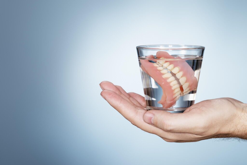 Man holding a glass containing old dentures.